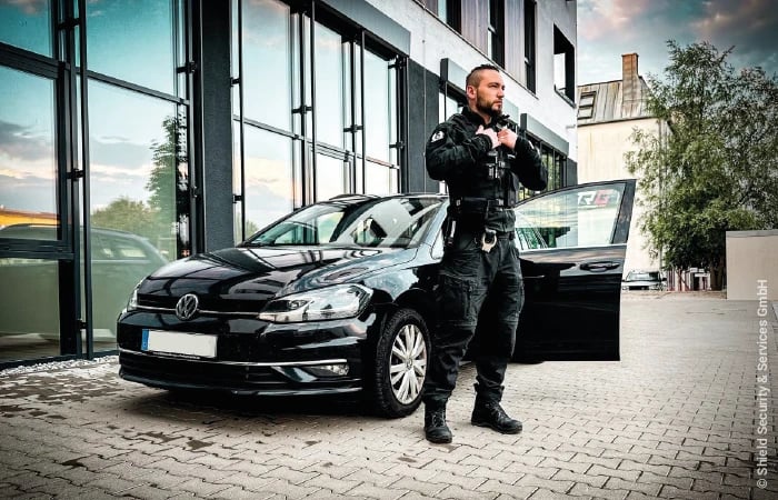 Shield Security & Services GmbH Sicherheitsmitarbeiter in Uniform steht vor Auto bei Objektschutz