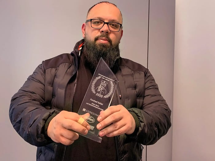 Farshad Safari hält die Trophäe für den „Sicherheitsmitarbeiter des Jahres 2025“ in den Händen und blickt in die Kamera.