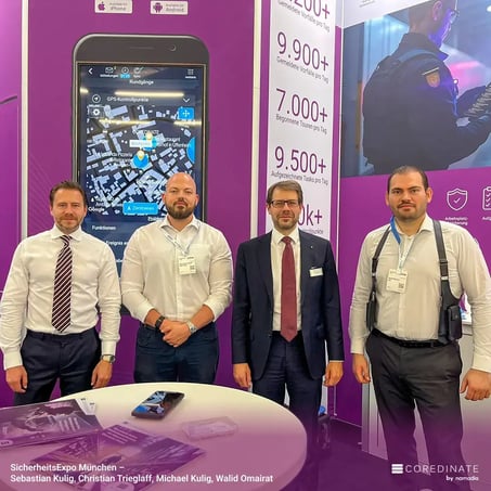 Sebastian Kulig, Christian Trieglaf, Michael Kulig, and Walid Omairat standing together at the COREDINATE® booth at SecurityExpo Munich, looking at the camera.