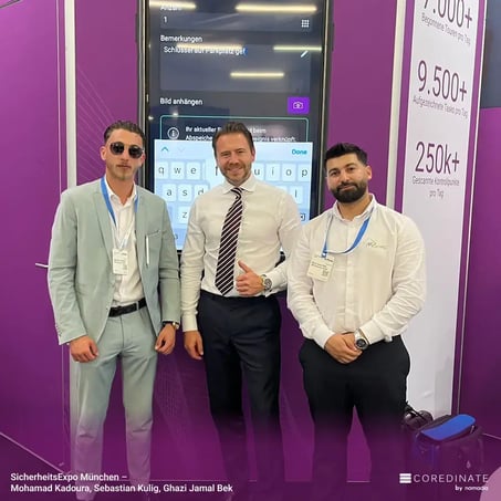 Mohamad Kadoura, Sebastian Kulig, and Ghazi Jamal Bek standing side by side, smiling at the camera at the COREDINATE® booth at SecurityExpo Munich.
