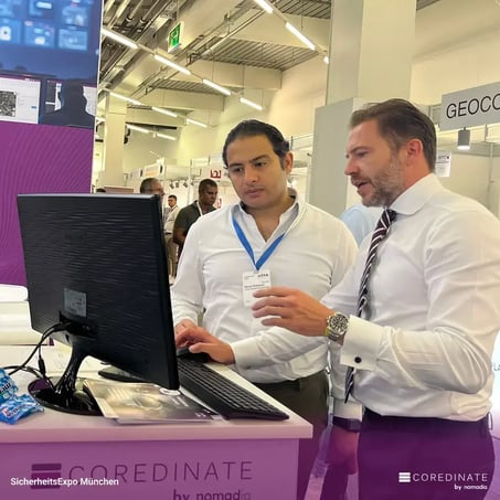 Sebastian Kulig explaining something on a computer screen to a visitor at the COREDINATE® booth at SecurityExpo Munich.