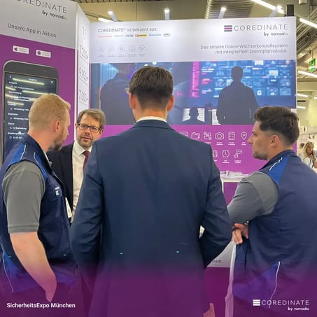 Four men, including Michael Kulig, Georg Meier, Fabian Becker, and Pierpaolo Nocera, standing with their backs to the camera talking at the COREDINATE® booth at SecurityExpo Munich.