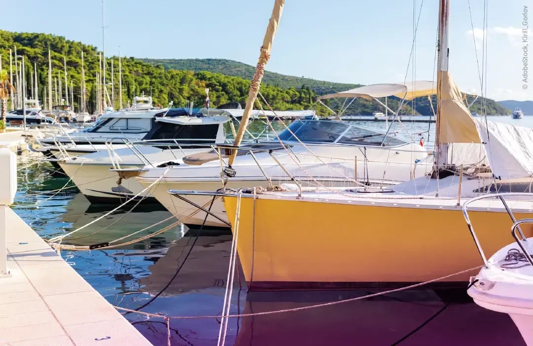 Boote liegen am Hafen an bei blauem Himmel und hügeliger Natur im Hintergrund