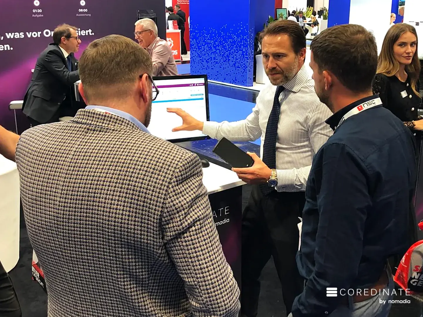 Sebastian Kulig zeigt zwei Besuchern die COREDINATE-App am Stand auf der Security Essen 2026