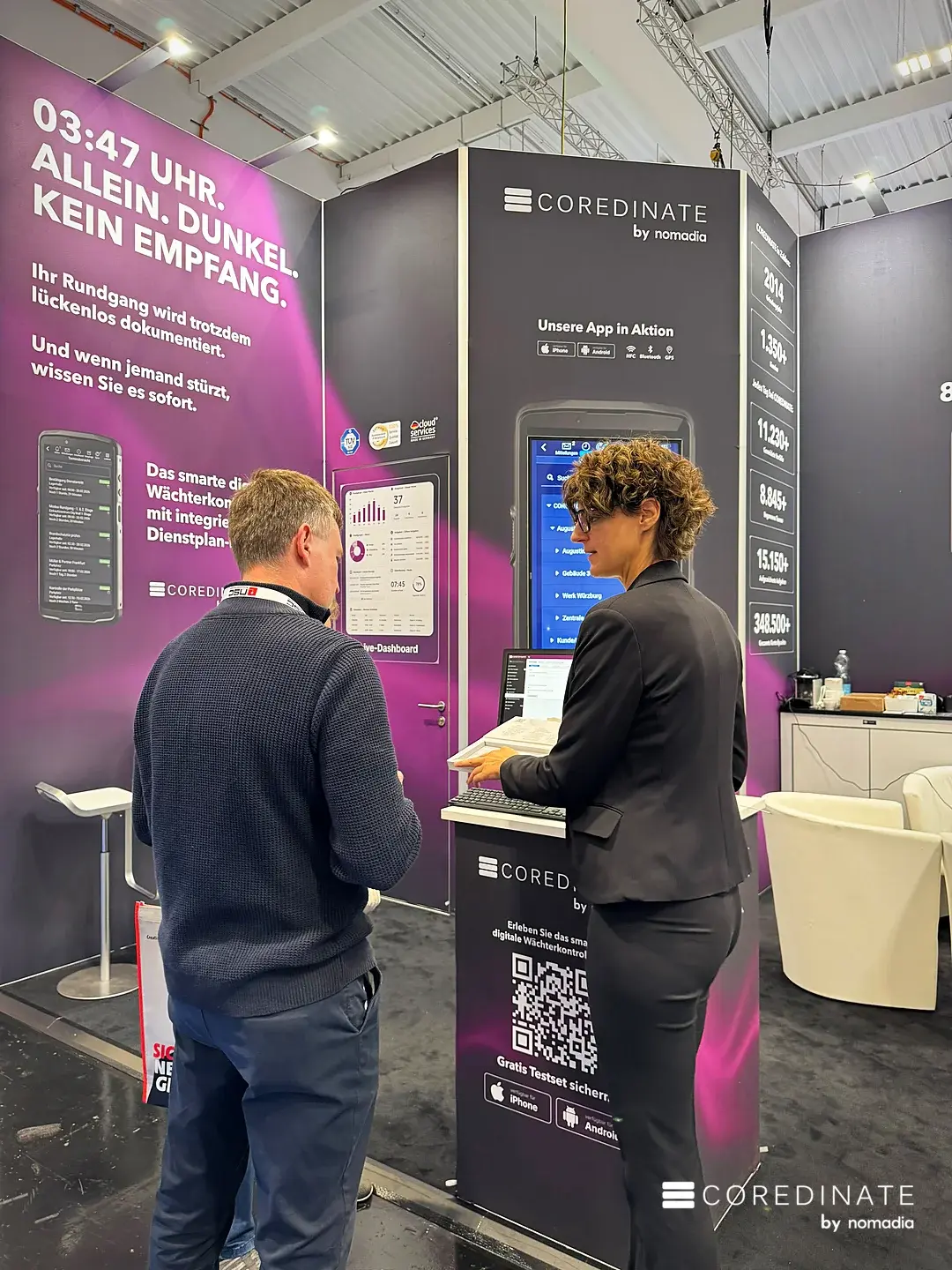 Gespräch am Demo-Platz vor der großen App-Anzeige des COREDINATE-Stands