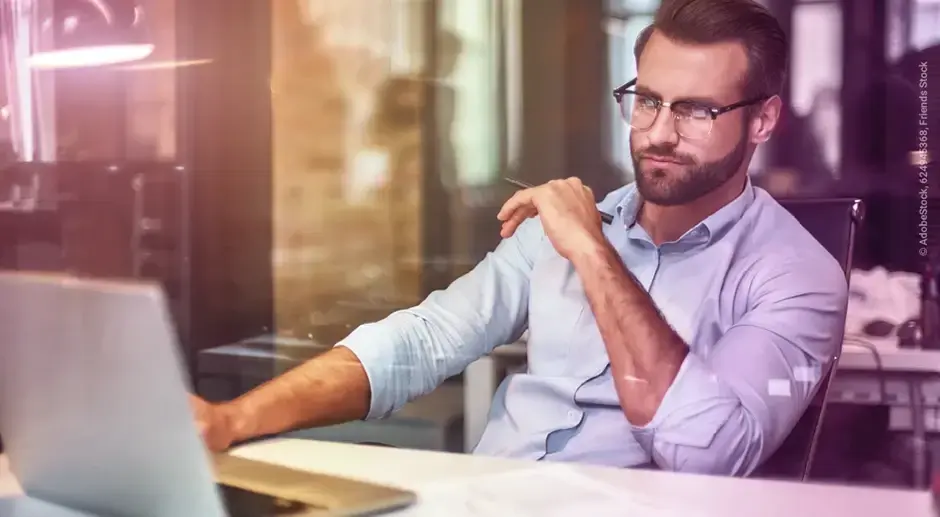 شاب رجل أعمال يجلس عند مكتبه وينظر إلى شاشة الكمبيوتر المحمول